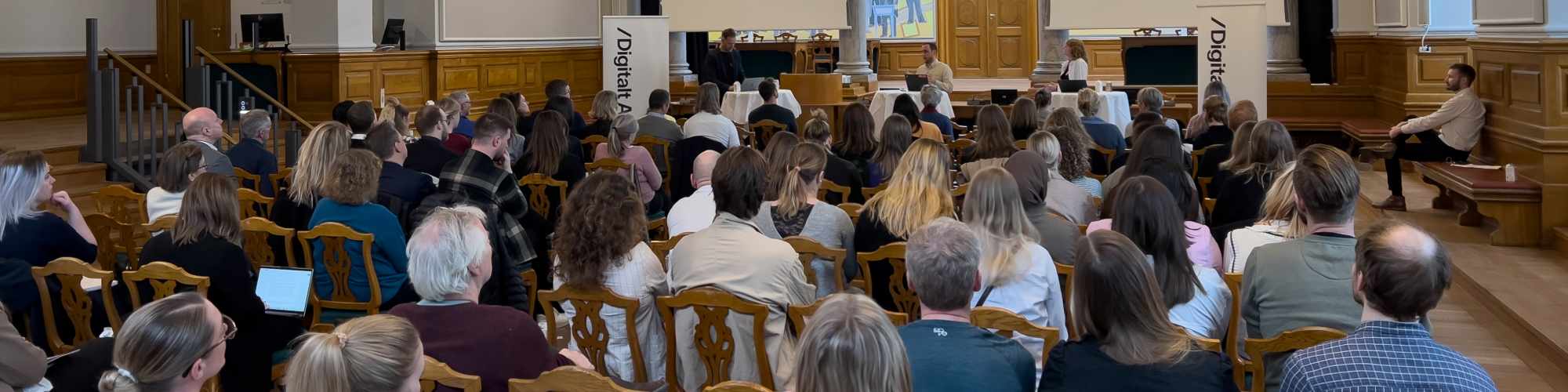 En samling mennesker sidder og lytter til et oplæg under en konference
