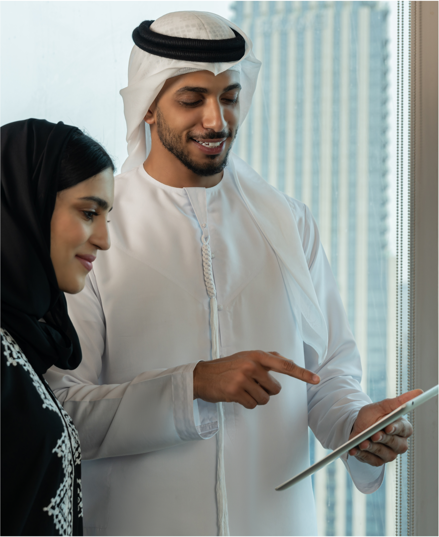 Two professionals in traditional Emirati attire reviewing information on a tablet in a modern office