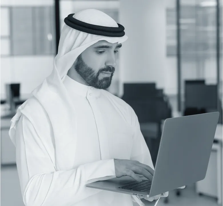 Man wearing traditional Middle Eastern attire working on a laptop in a modern office.