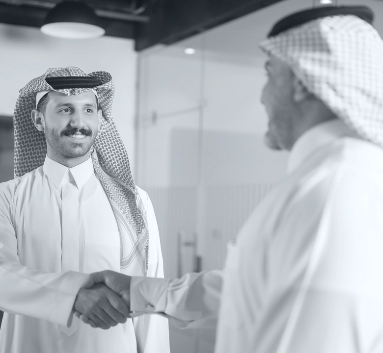 Two men in traditional Middle Eastern attire shaking hands and smiling in an office setting.