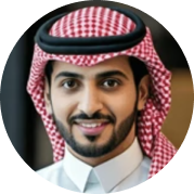 Smiling man wearing a traditional red and white checkered keffiyeh and white thobe.