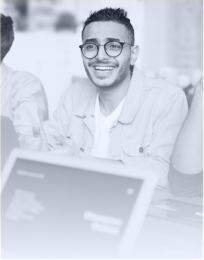 Smiling man with glasses sitting at a desk with a laptop.