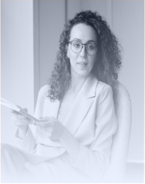 Woman with curly hair and glasses sitting on a chair, holding papers.