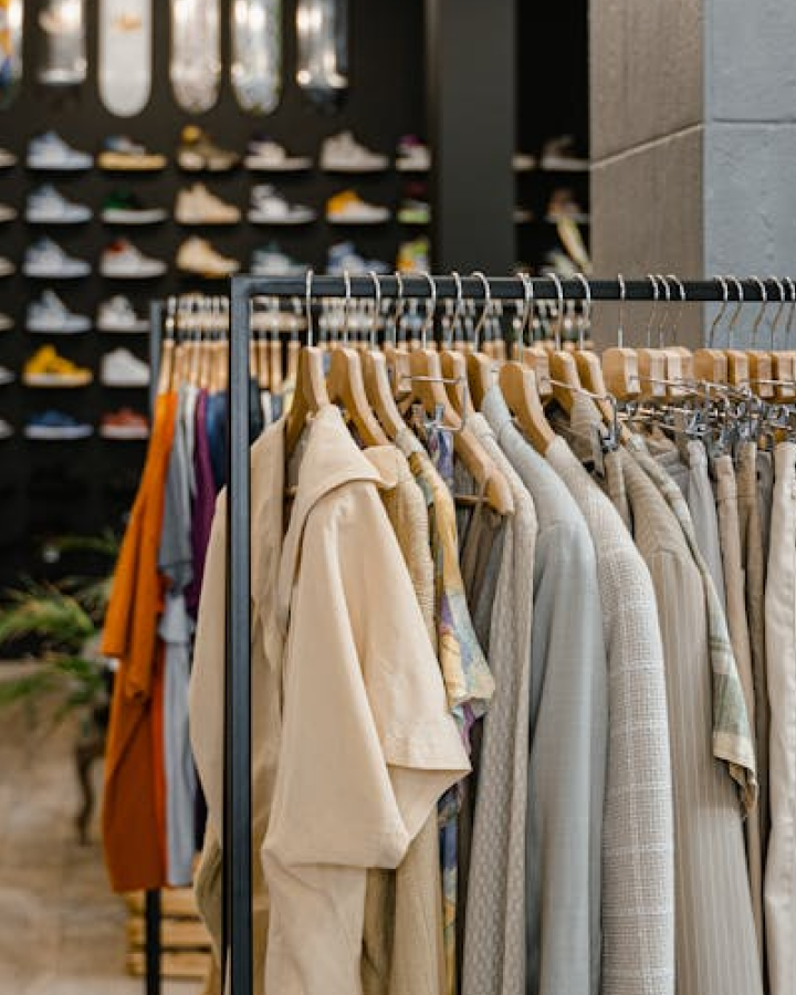 Clothing rack with neutral-toned shirts and jackets in a retail store, with shelves of shoes blurred in the background.