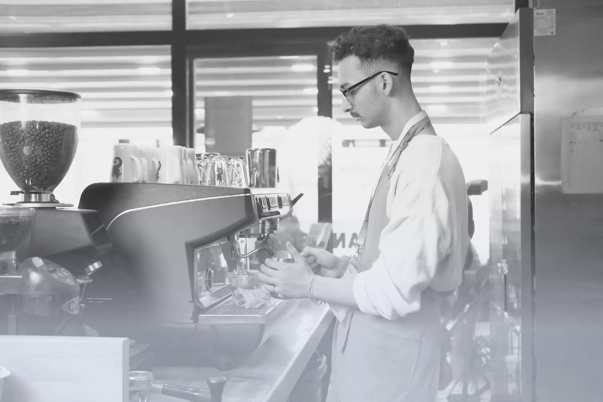 Barista in apron preparing coffee using an espresso machine in a café.