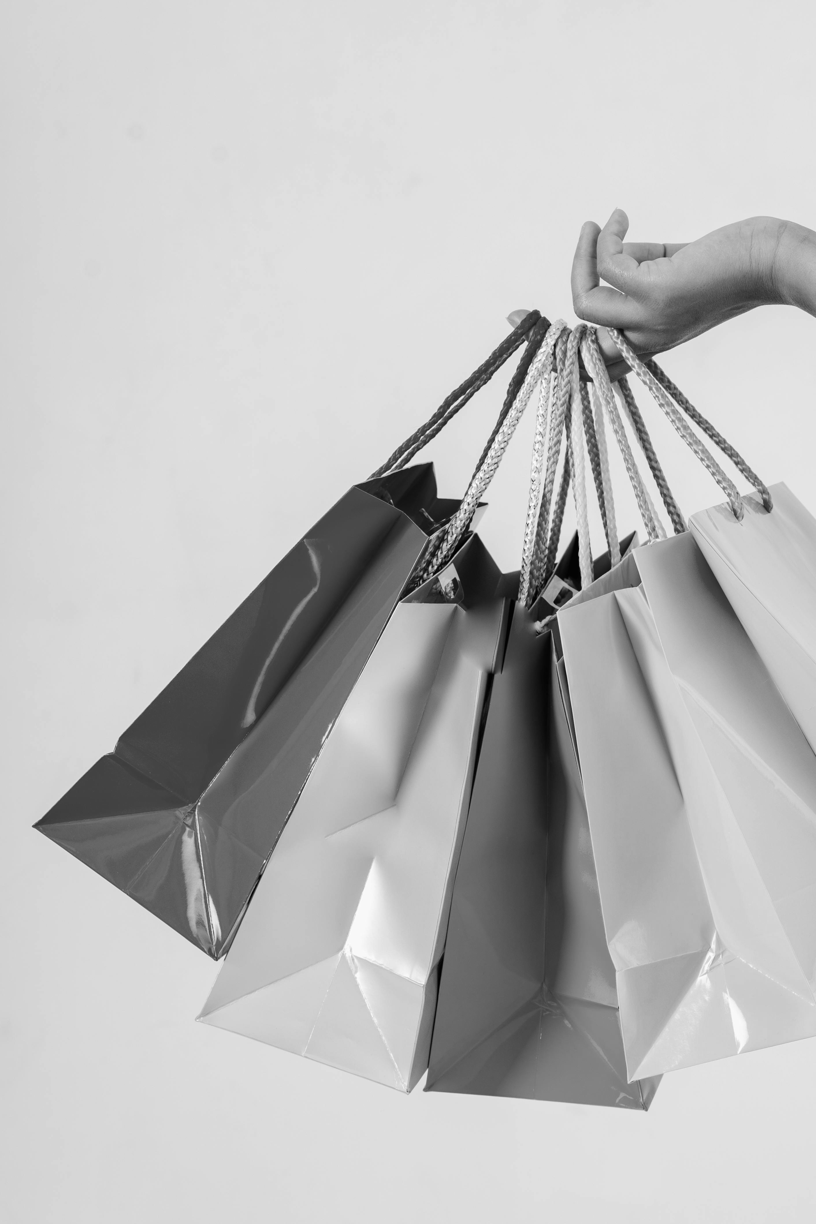 Hand holding several glossy shopping bags with braided handles against a plain background.
