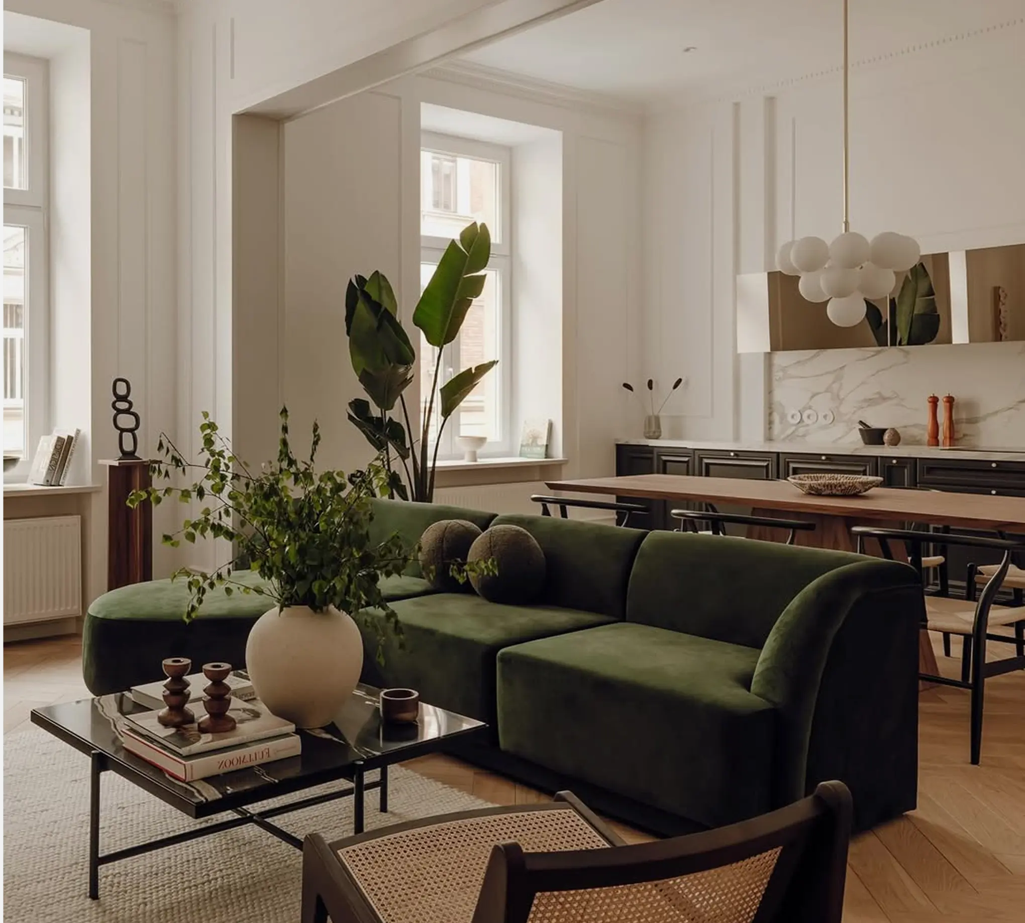 Modern living room with a green sofa and a decorative vase, overlooking a bright open kitchen.