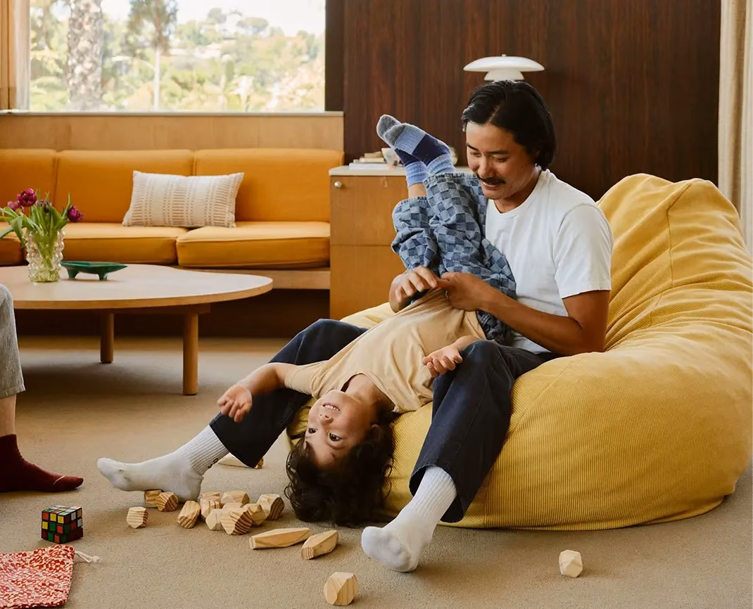 Father playing with his young son on a yellow beanbag at home