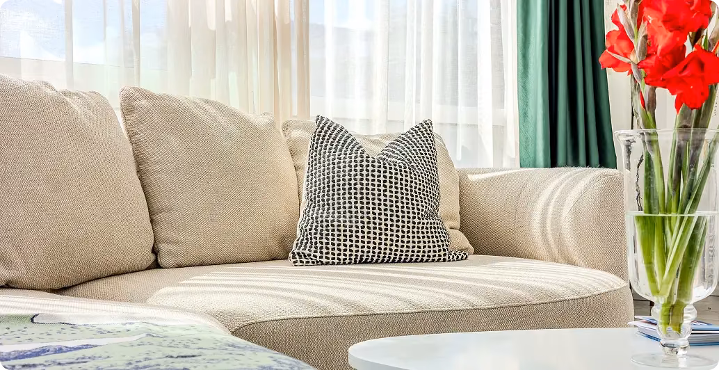 Close-up of a cream sofa with a patterned cushion beside red flowers in a vase