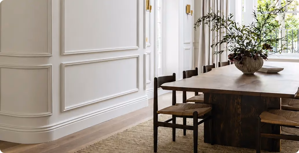 White panelled dining room with a rustic wooden table, rush chairs and a branch vase
