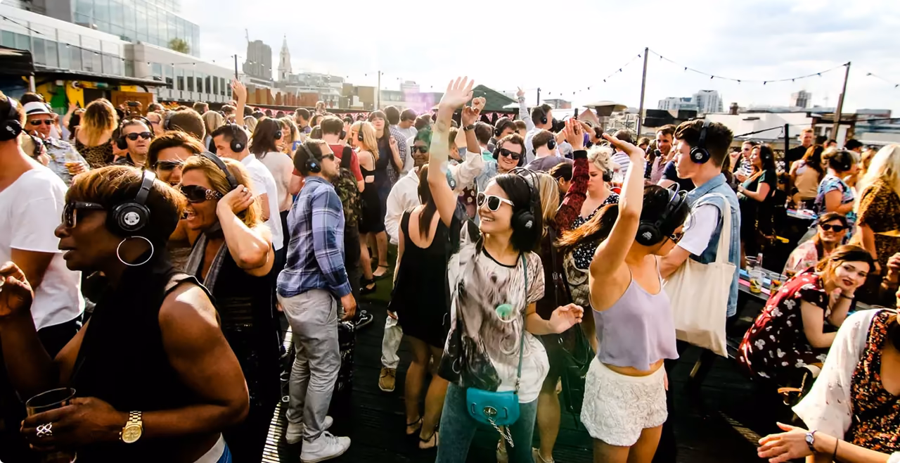 Crowd of people with headphones dancing at a sunny rooftop silent disco party