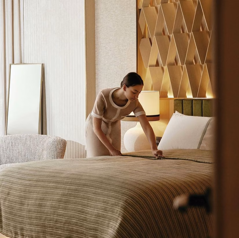 Housekeeper smoothing a striped bedspread in a bedroom with a patterned headboard wall