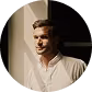Portrait of a man in a light shirt looking to the side against a dark background.