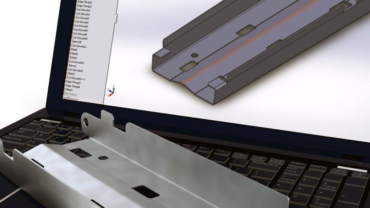a sheet metal part rests on a laptop with a 3D model of the part on the screen