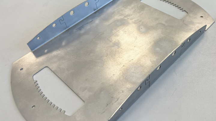 a cut, bent, and deburred sheet metal part on a white surface