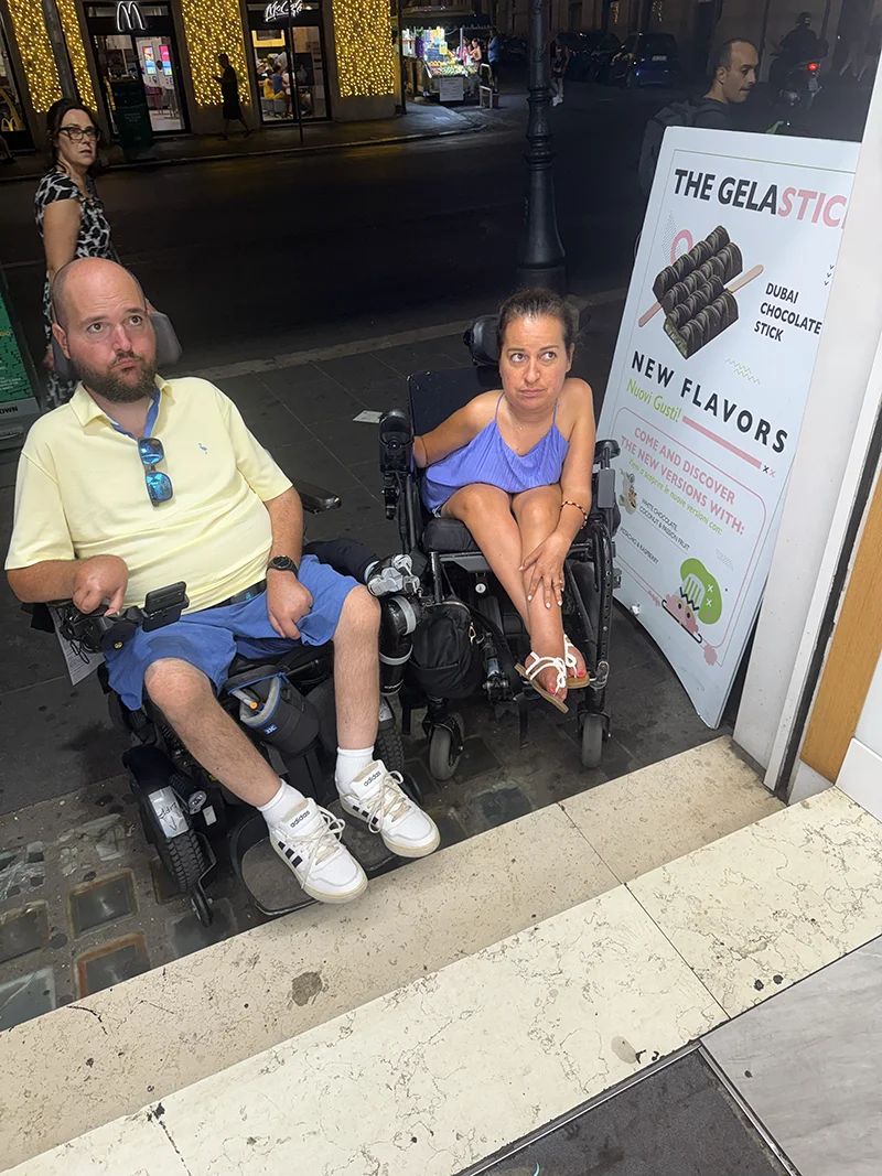 Two people in wheelchairs with sad faces sitting at the bottom of steps
