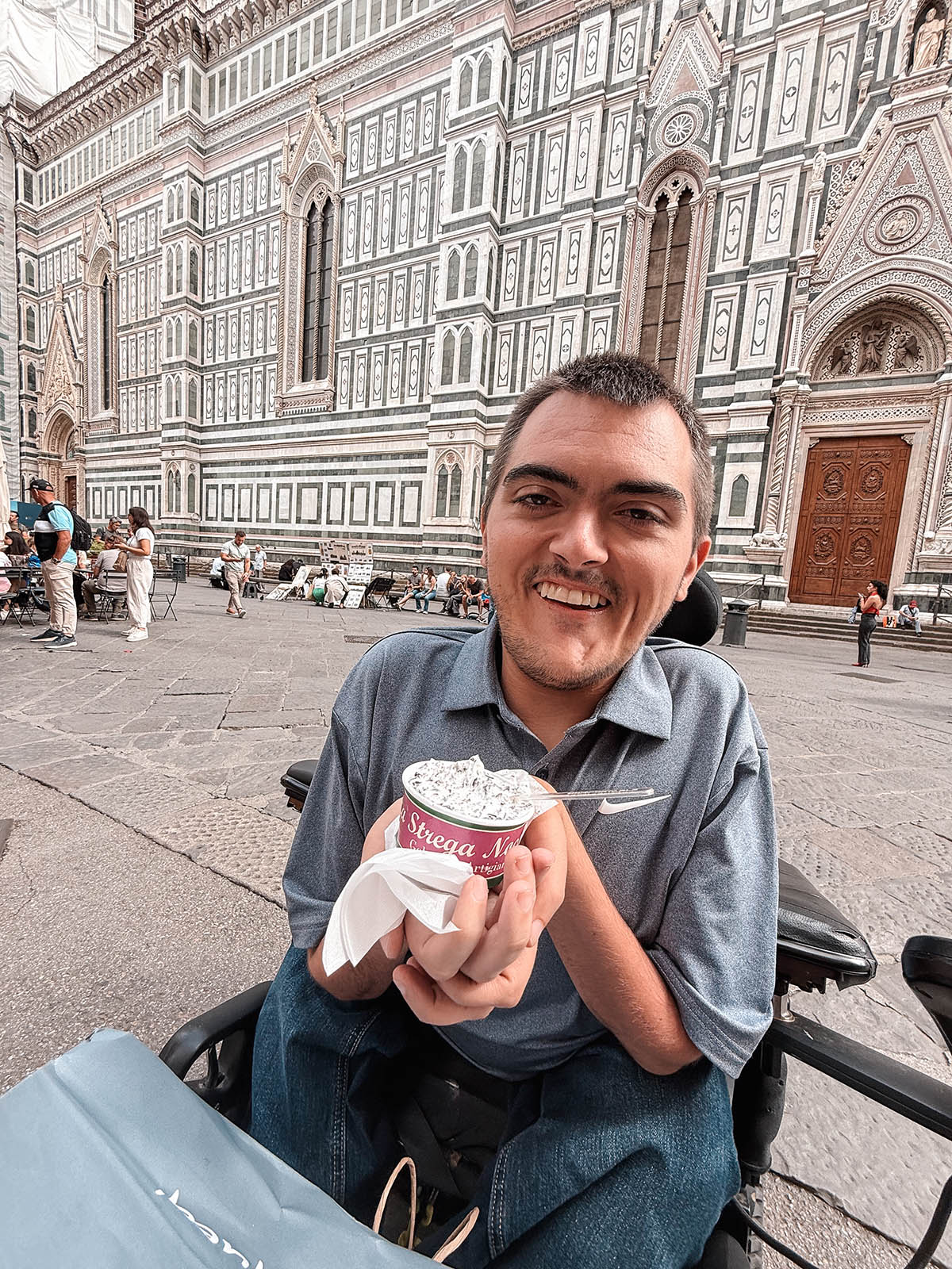 man in wheelchair smiling holding gelato cup with the Duomo in the background