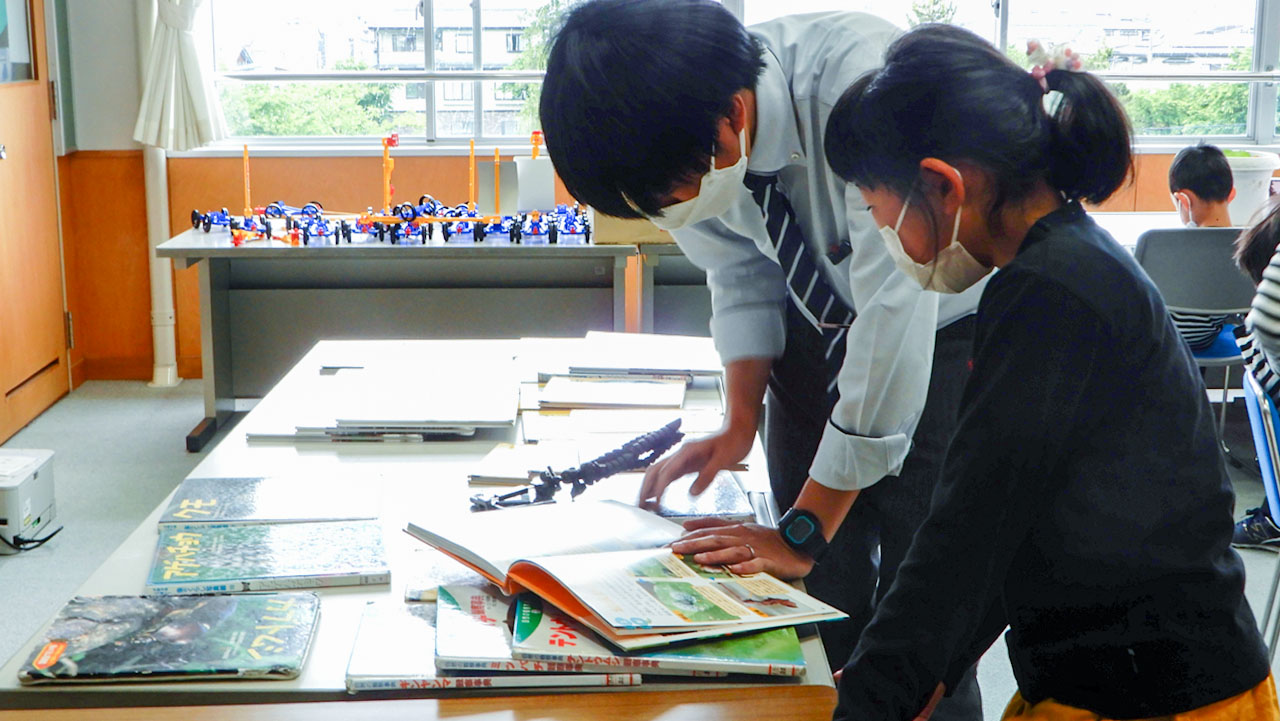 関連する書籍を見ながら、質問に来た子供の話を聞く教員