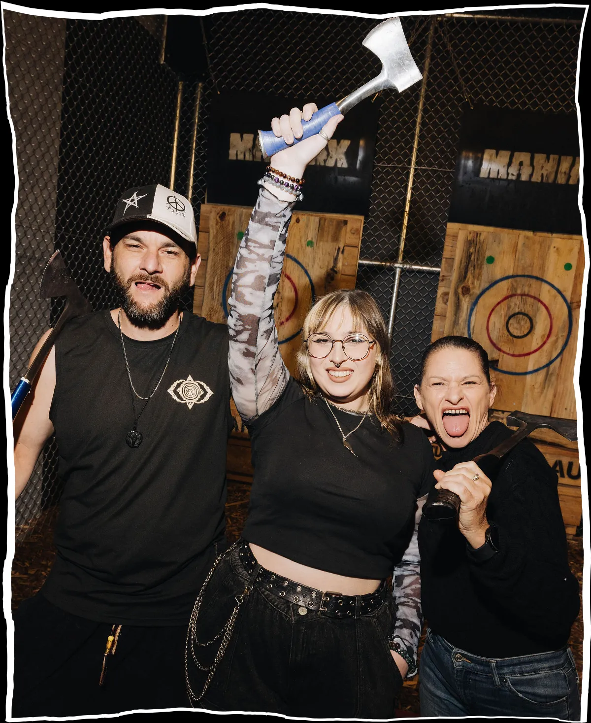 Smiling woman in black cropped shirt and ripped jeans holding an axe at an axe throwing venue.