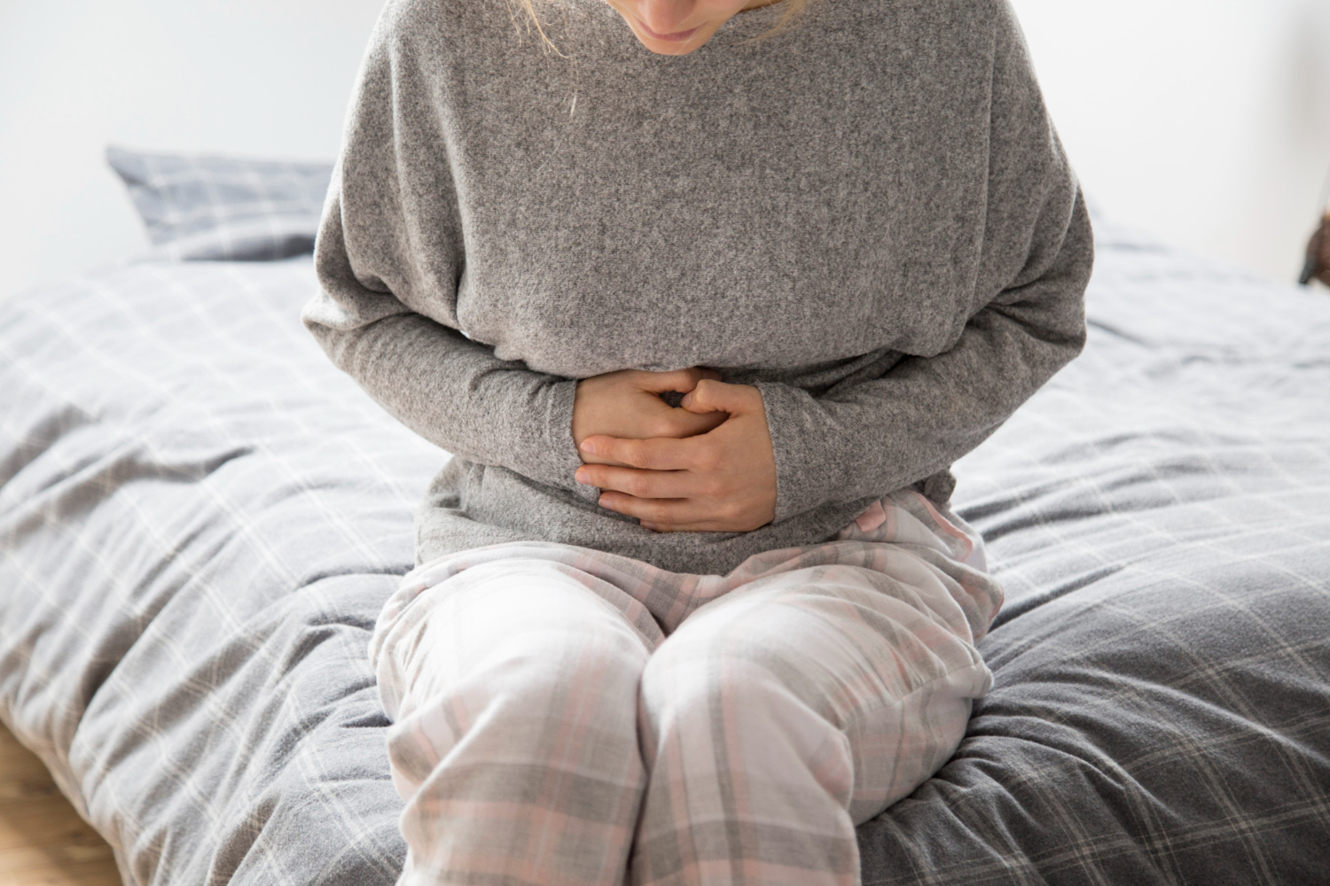A woman sits on a bed, holding her stomach as if she's in pain.
