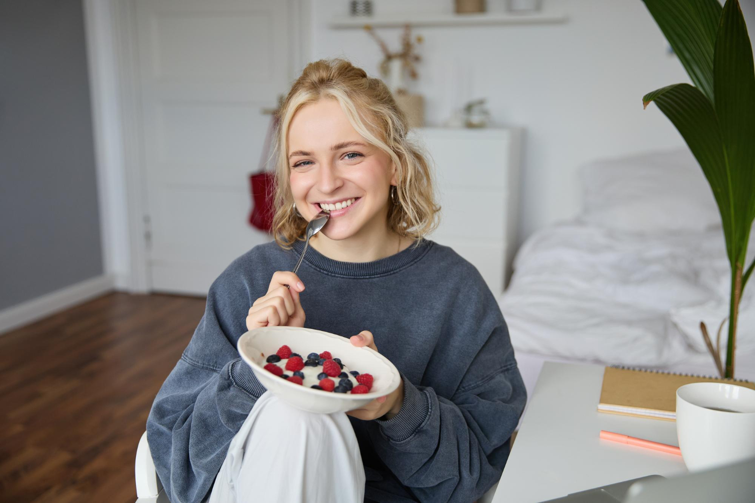 A woman smiles at the camera while enjoying a healthy breakfast of yogurt and berries.