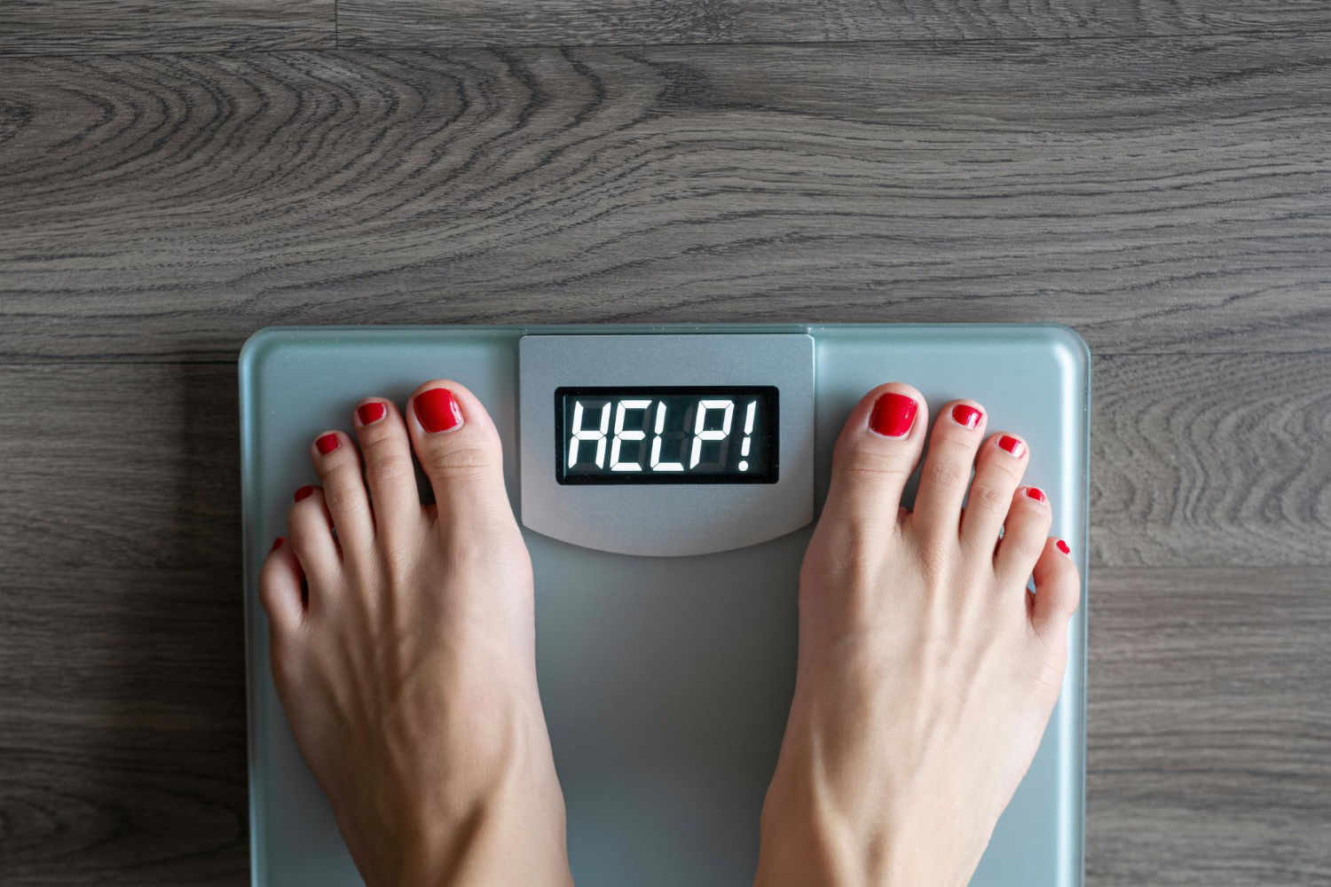 An image of a woman's feet on a scale. The screen of the scale reads "HELP!"