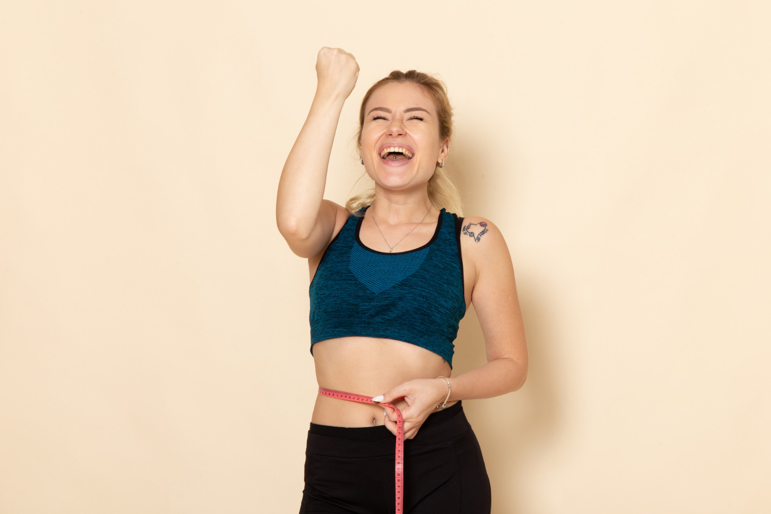 A woman celebrates hitting a weight loss goal as she measures her waist with a tape measure.