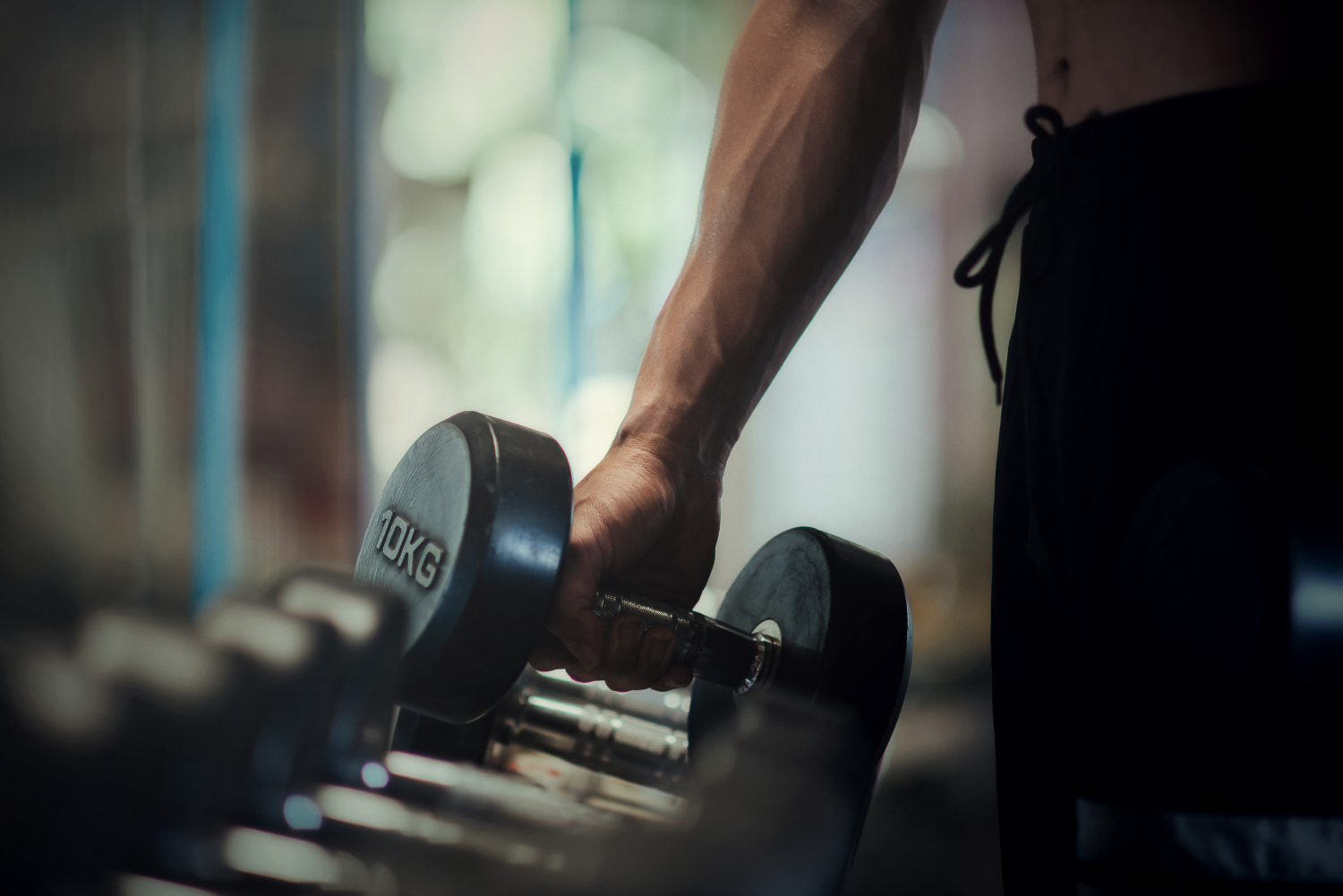 A man picks up a large weight from a rack of weights in a gym.