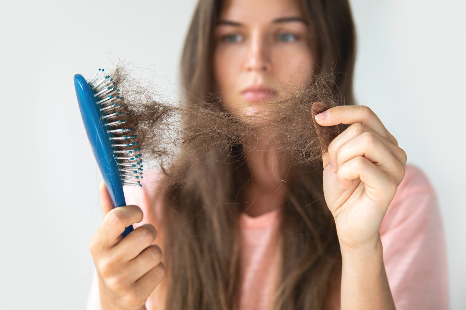 A woman pulls clumps of hair from a hair brush.