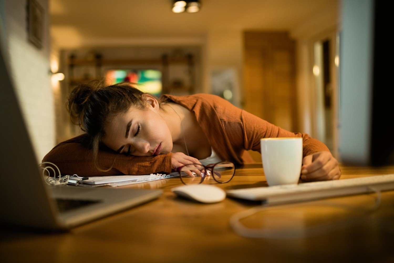 A woman lays her head down at her desk during a long, exhausting workday.