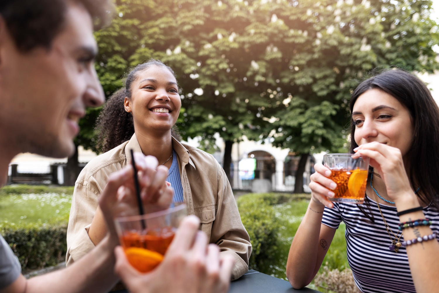 Three friends enjoy cocktails outside on a sunny day.