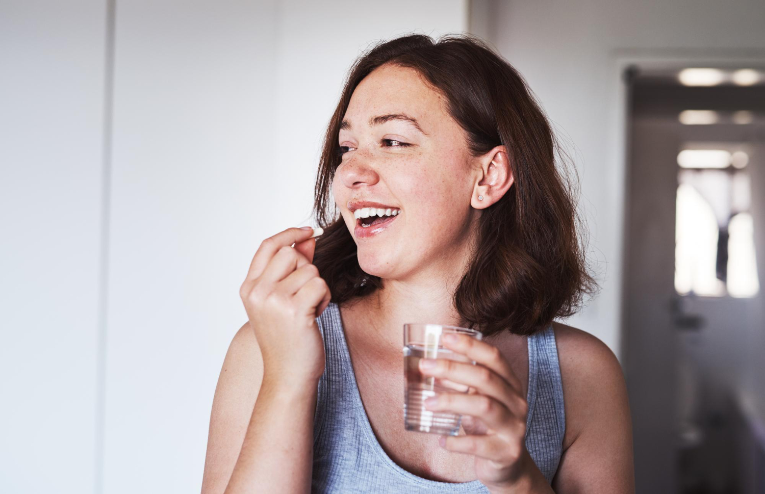 A woman takes a small white pill with a glass of water.