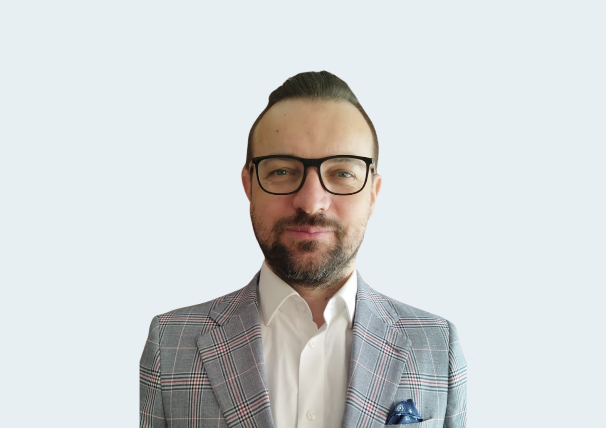 Mężczyzna z brodą i okularami w garniturze w kratę i białej koszuli na jasnym tle.