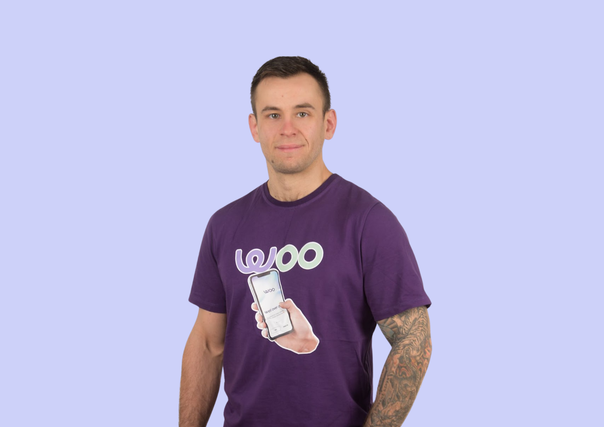 Mężczyzna w fioletowej koszulce z nadrukiem telefonu i logo WOO na jasnofioletowym tle.