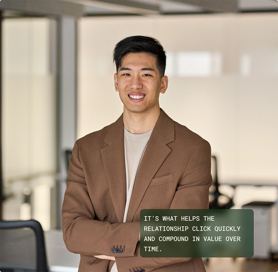 A smiling young man in a brown blazer stands in an office setting with his arms crossed. A green text box overlays the bottom right with a quote about relationships compounding in value.