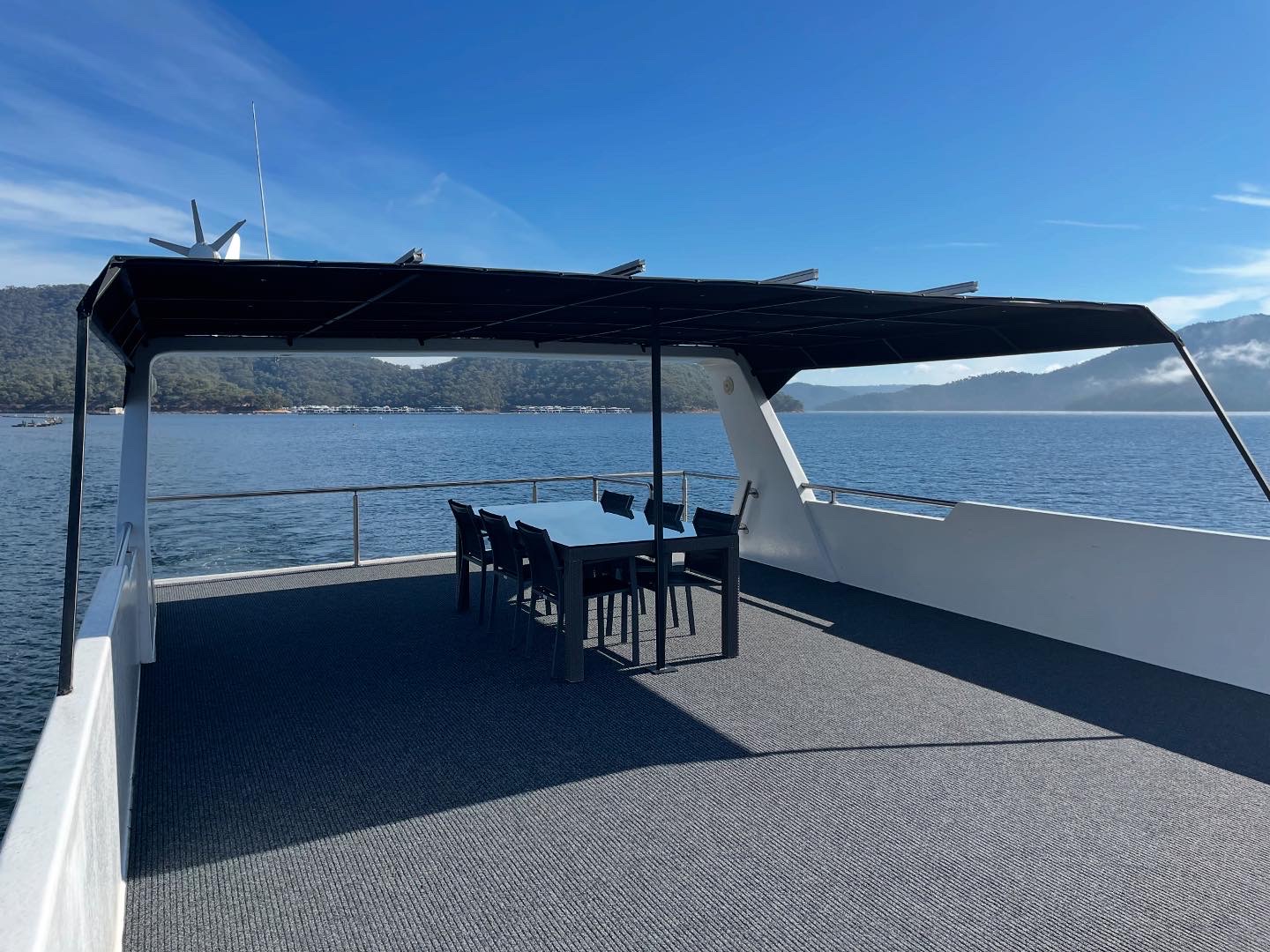 Covered rooftop deck with a dining table and chairs under a shade canopy with solar panels, overlooking the lake and hills.