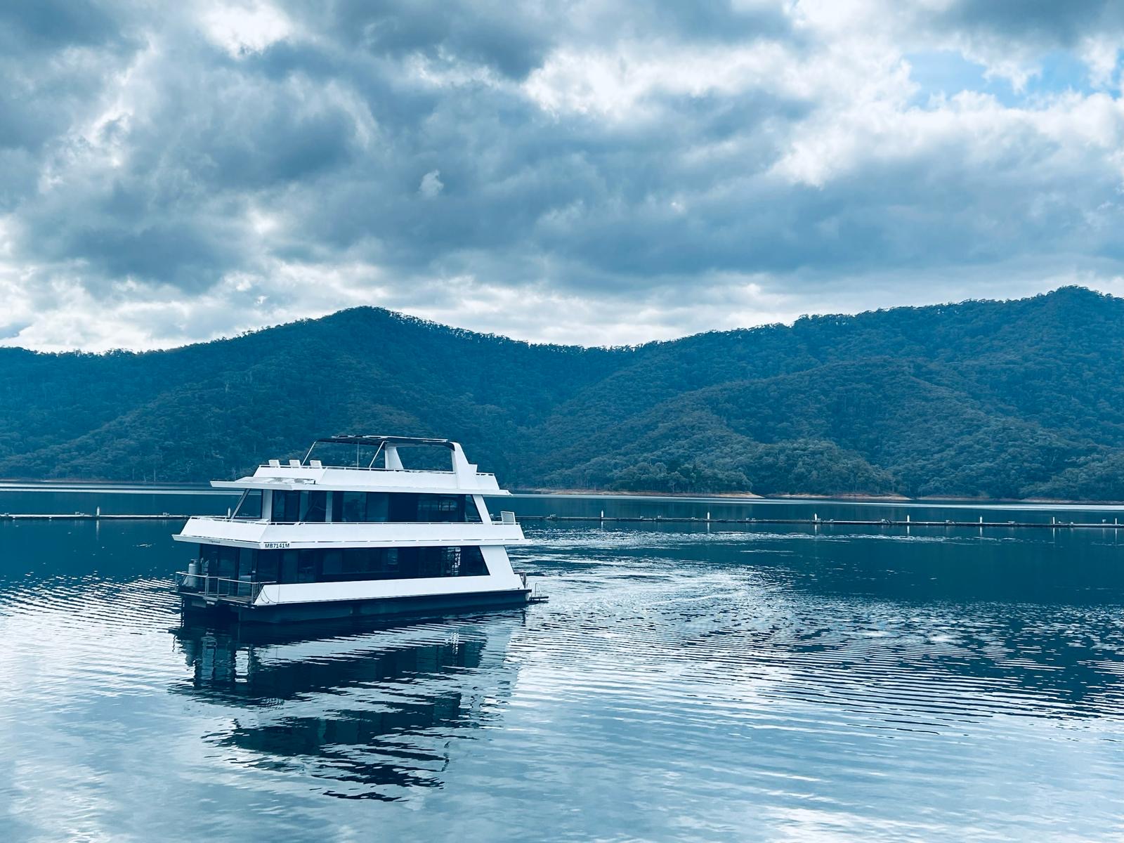 The Diplomat houseboat moored on calm water under a moody, cloud-filled sky with forested hills behind.