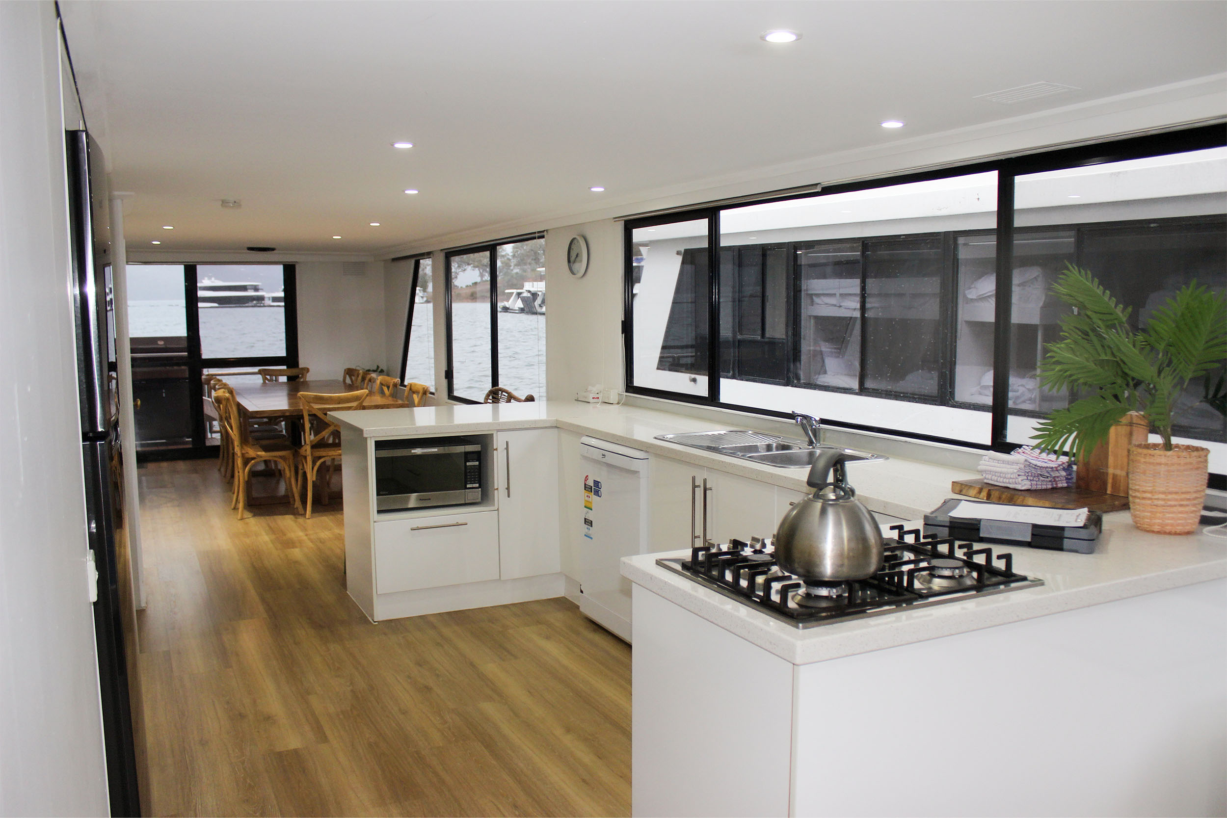 Open-plan kitchen with white cabinetry, gas cooktop and a dining area with wicker chairs, lake view through the windows.