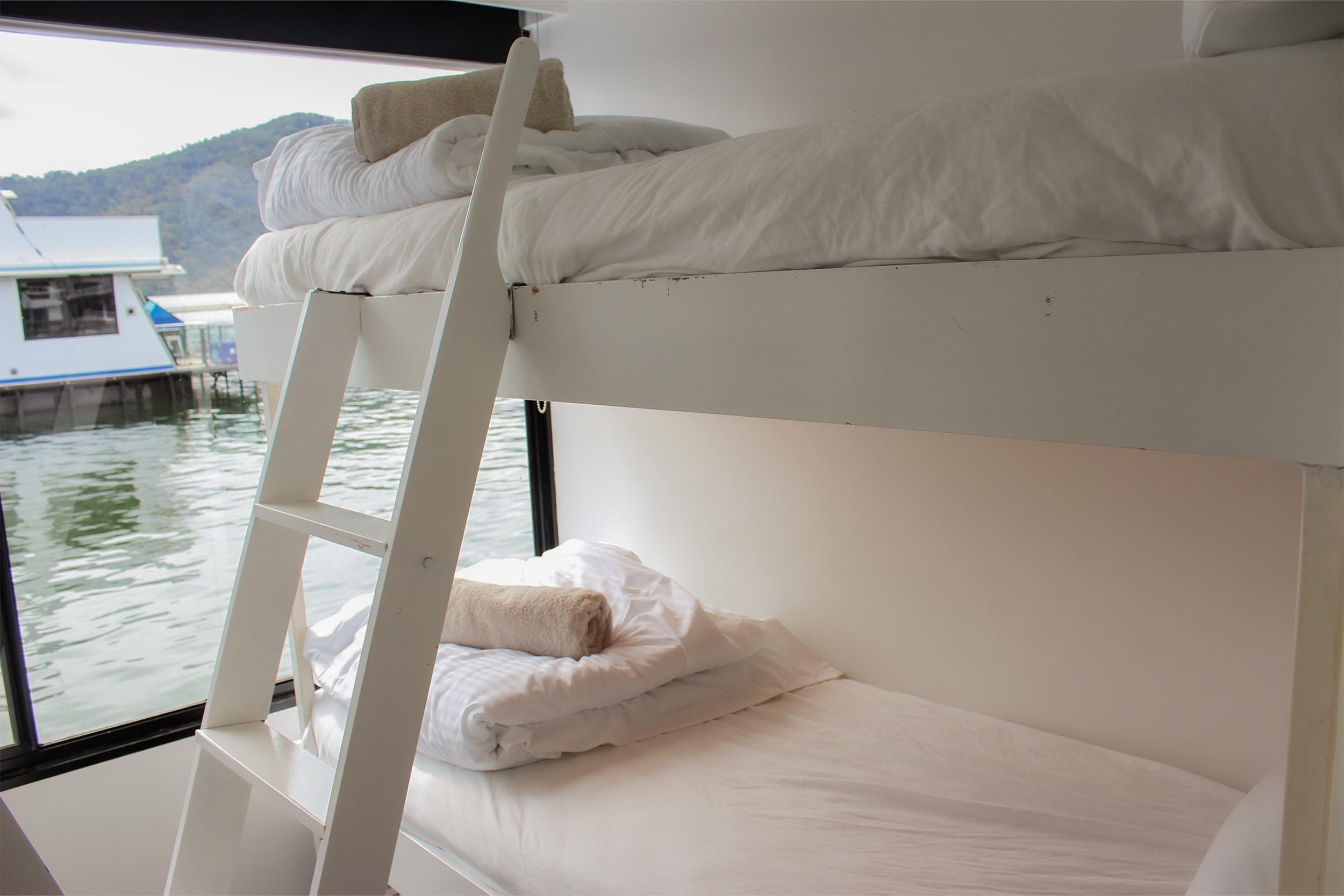 Bunk beds with a white ladder, window view of a neighbouring houseboat and the lake.