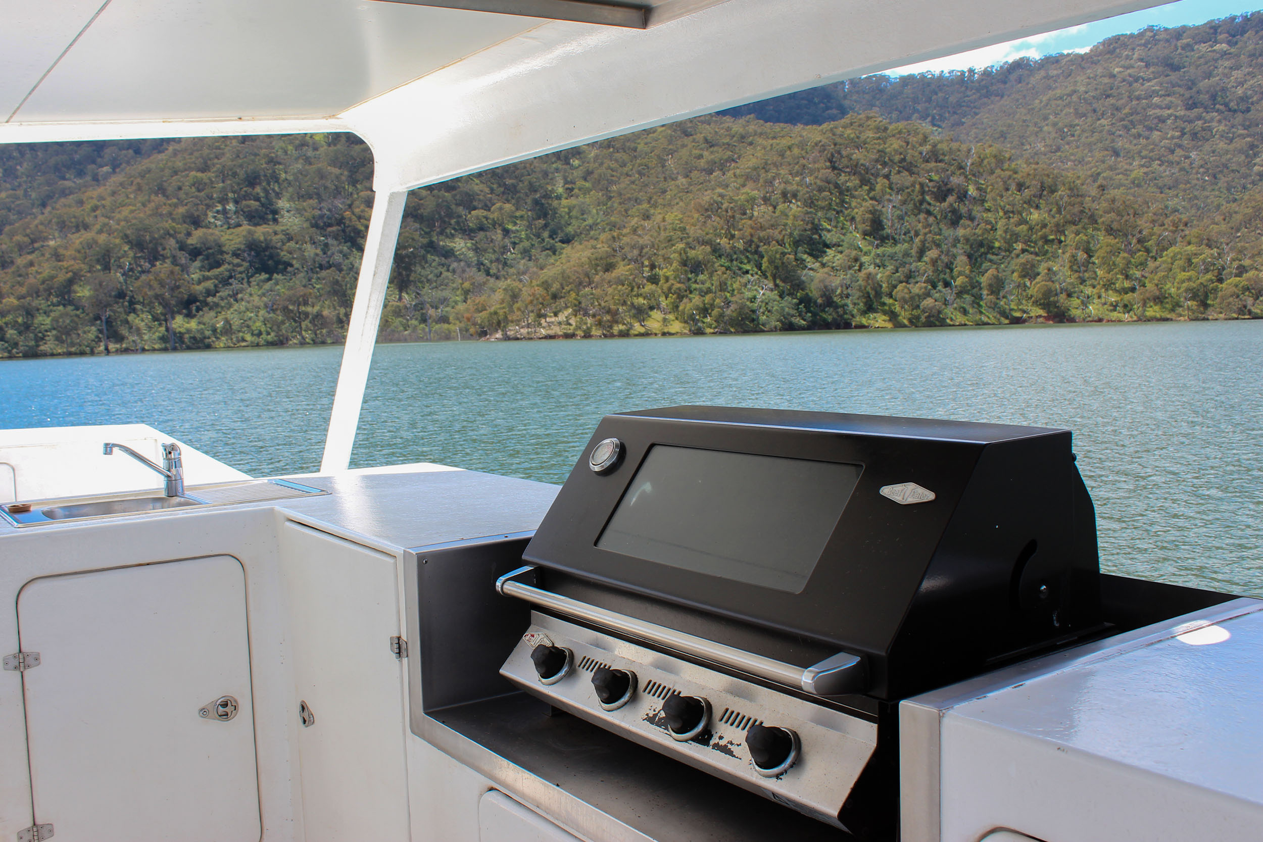 Outdoor BBQ area on the rooftop deck with a sink and gas BBQ, overlooking the lake and forested hills.