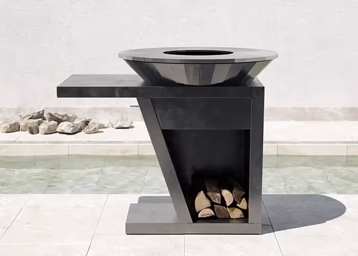 Barbecue moderno da esterno in metallo nero con piano laterale integrato, vano porta legna inferiore e braciere circolare, posizionato accanto a una piscina.