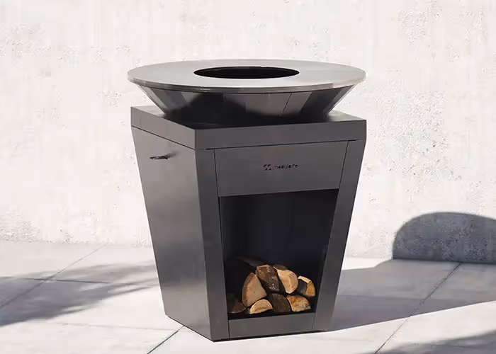 Barbecue moderno da esterno color antracite con piastra di cottura circolare e vano portalegna inferiore.