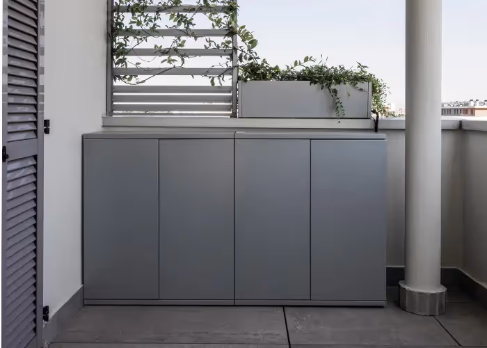 Mobile contenitore grigio a quattro ante installato sul balcone di un terrazzo sotto una fioriera.