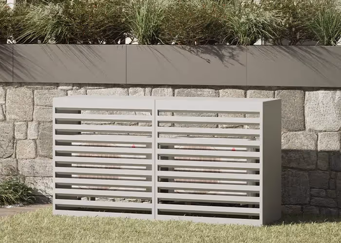 Copertura moderna per unità esterna con struttura metallica grigio chiaro a doghe orizzontali, posizionata in un giardino davanti a un muro in pietra e una fioriera con vegetazione.