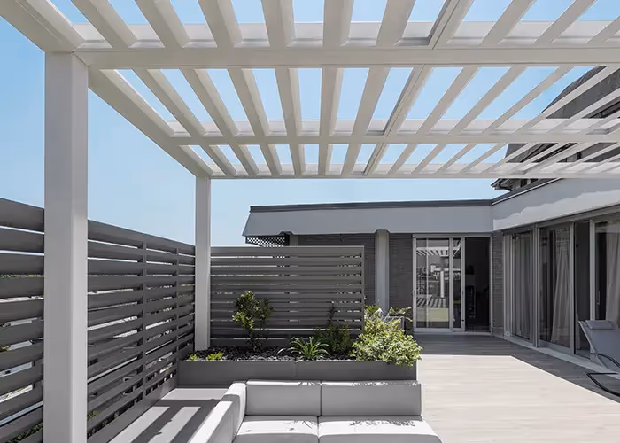 Ampio terrazzo moderno con pergola bioclimatica bianca, fioriere grigie con divano integrato e facciata vetrata.