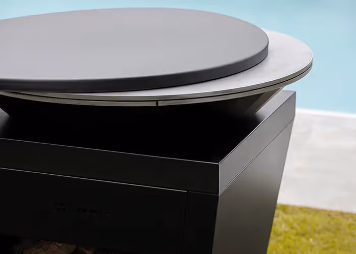 Dettaglio del piano circolare di un barbecue moderno da esterno in metallo nero con superficie di cottura rialzata.