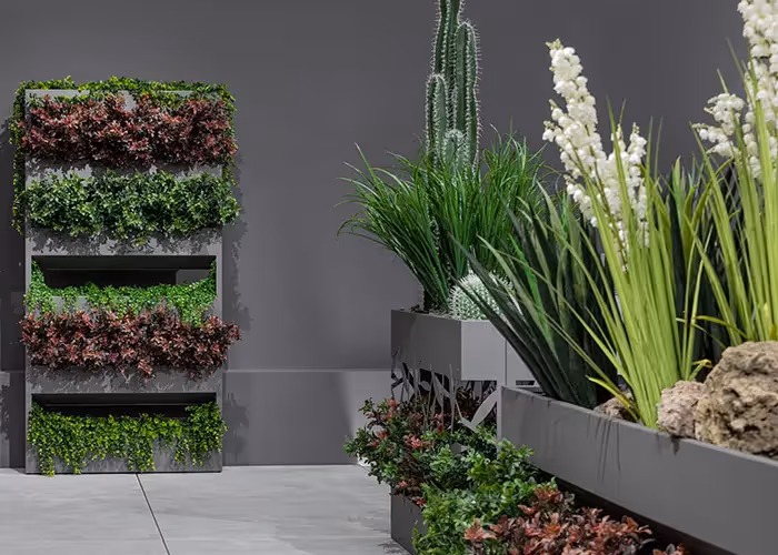 Composizione di fioriere moderne e giardino verticale modulare con vegetazione ornamentale in uno spazio espositivo dal design contemporaneo.