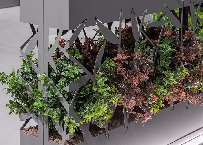 Dettaglio ravvicinato di una fioriera moderna grigio scuro con pannello traforato decorativo e vegetazione ornamentale.