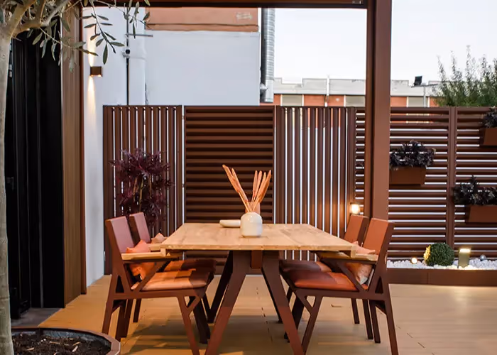 Tavolo da pranzo in legno e sedie su un patio esterno, delimitato da pannelli frangivista coordinati.