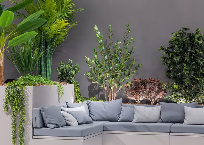 Divano modulare da esterno con cuscini grigi e grandi fioriere integrate contenenti piante decorative verdi, su sfondo minimalista scuro.